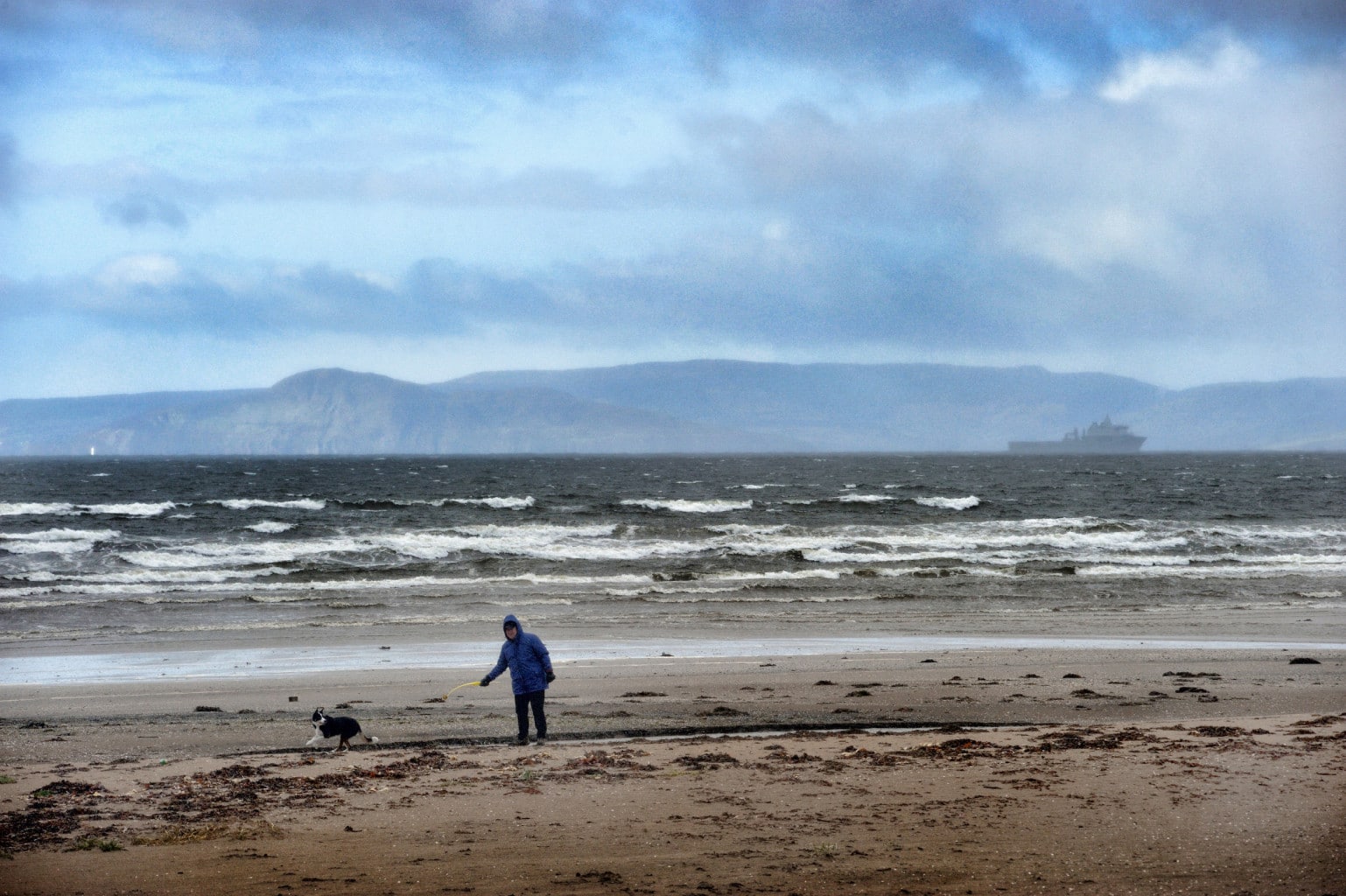 man walking his border collie on a windy and wet beach at Ardrossan, Scotland